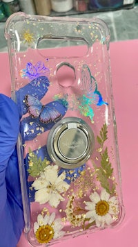 a woman is holding a phone case with butterflies and daisies on it
